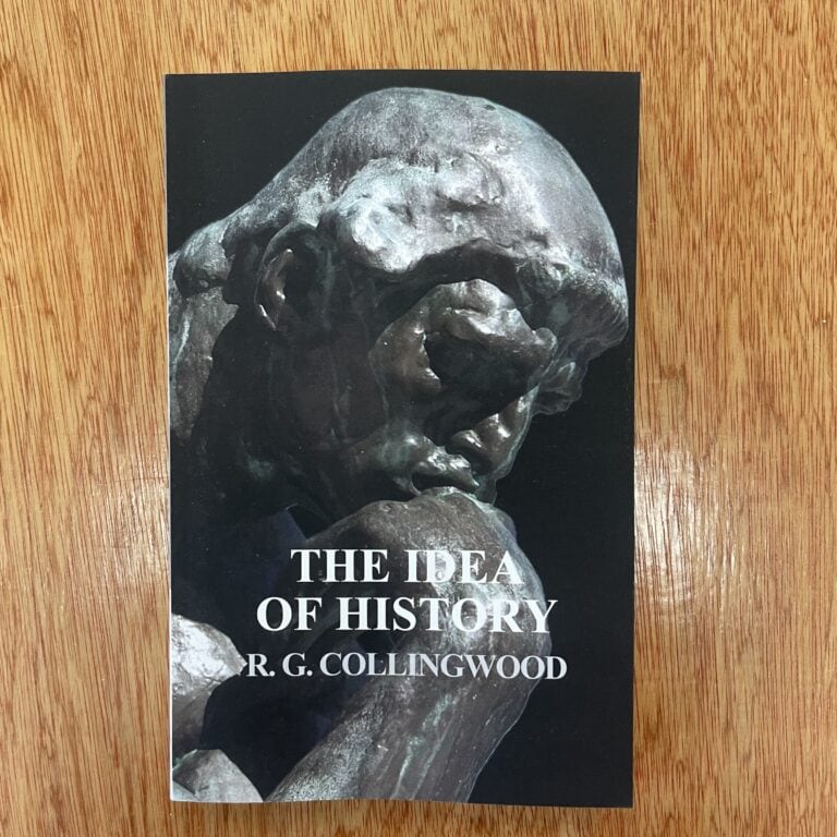 Close-up of 'The Idea of History' book by R.G. Collingwood on a wooden surface.